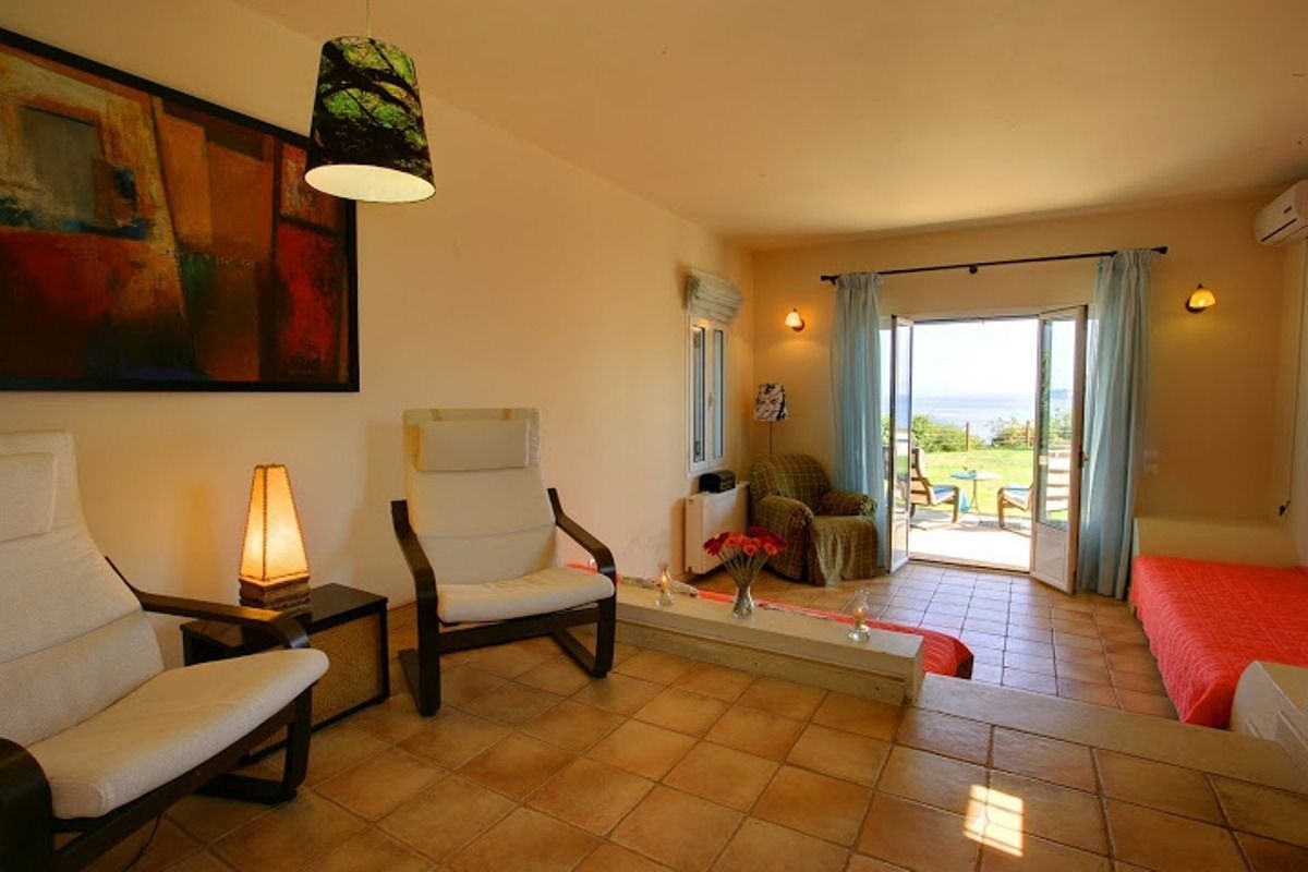A room with a sofa, chairs, a table, a lamp, a painting, and a view of the outdoors.
