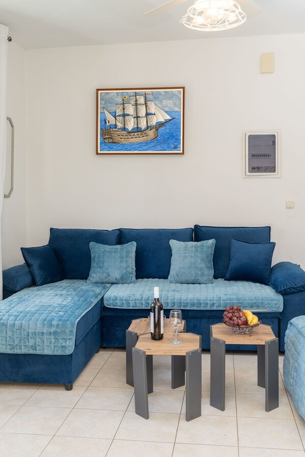 Una sala de estar moderna con un sofá azul, una mesa de centro de madera y una obra de arte enmarcada con un barco velero.