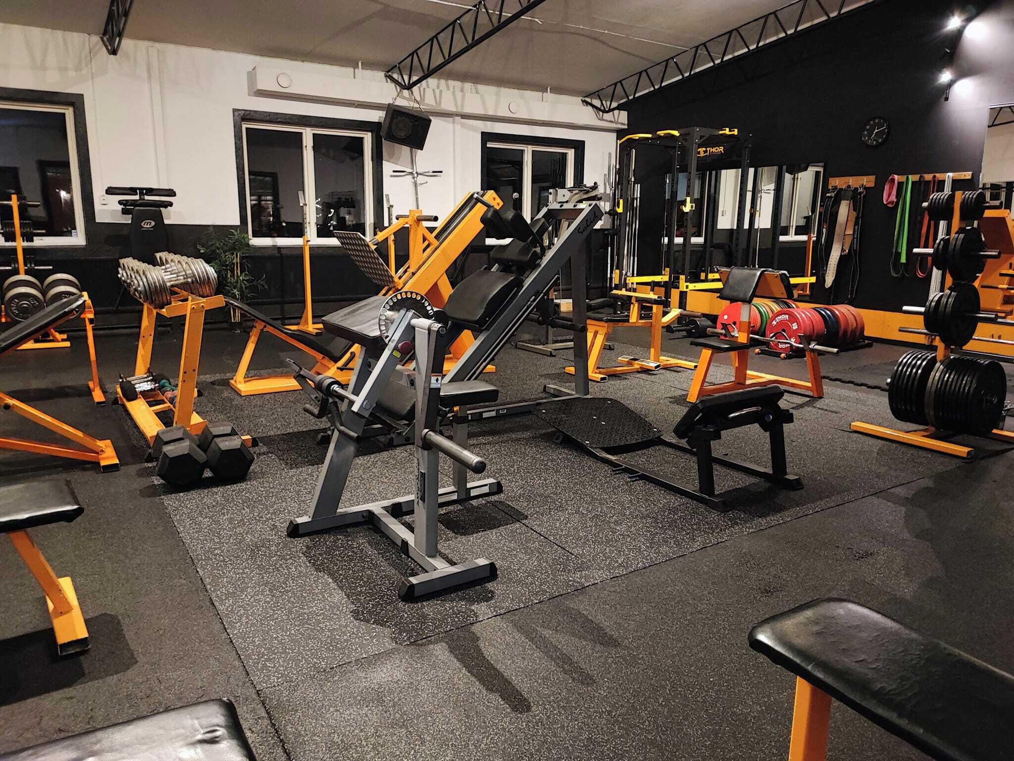 Un gimnasio con diferentes equipos de ejercicio, como mancuernas, discos de pesas y un banco.
