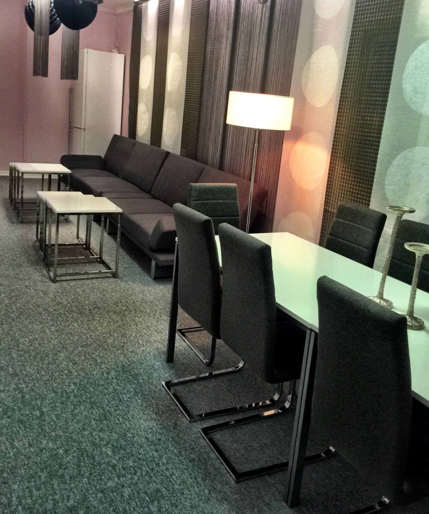 Een moderne vergaderruimte met een bank, tafels, stoelen en een lamp.