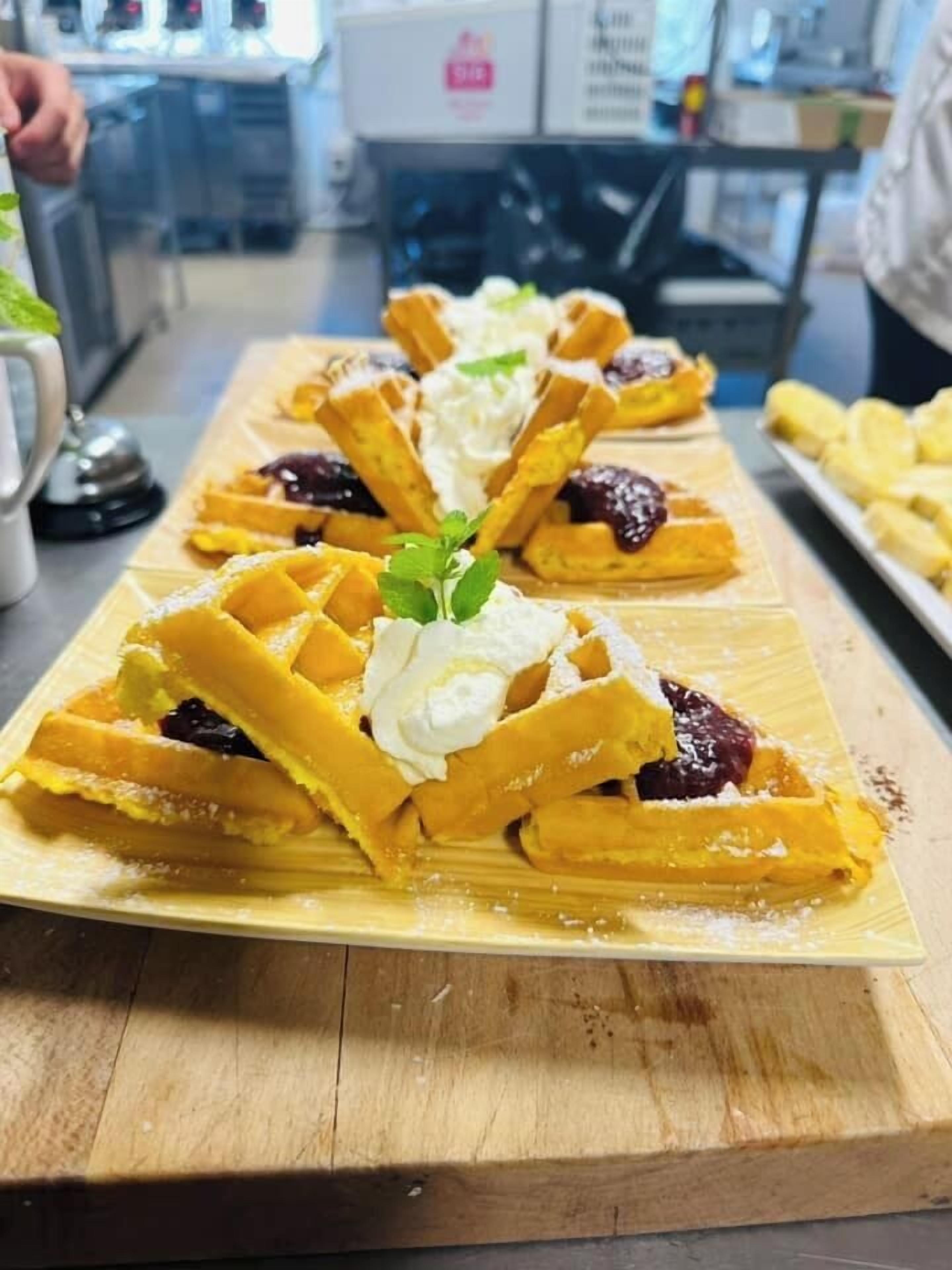 Una bandeja de gofres con crema batida y frutas encima de una mesa de madera en una cocina.