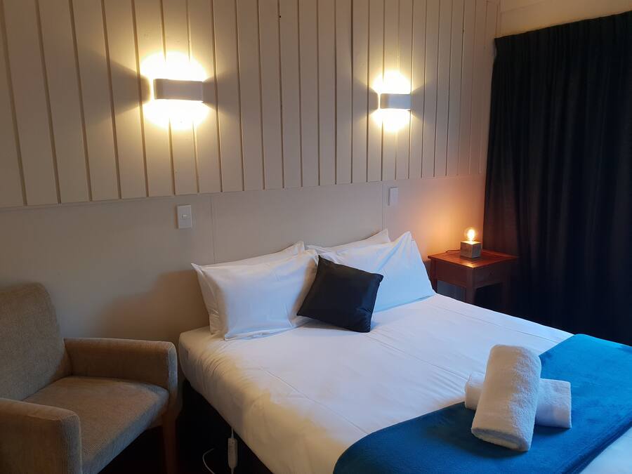 A hotel room with a bed, a chair, a nightstand, and two wall-mounted lights.