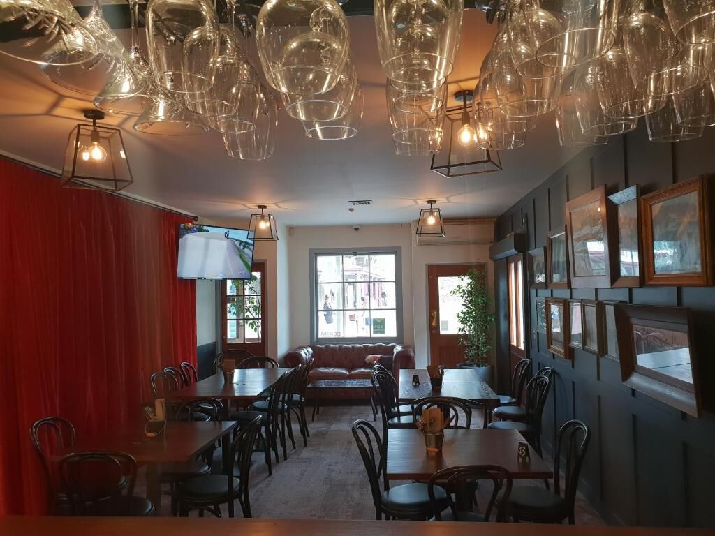 Un restaurante con varias mesas y sillas, una cortina roja en un lado y cuadros en la pared.