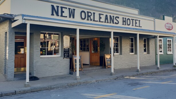 Exterior del Hotel New Orleans con un letrero, una pequeña tienda y vista de la calle.