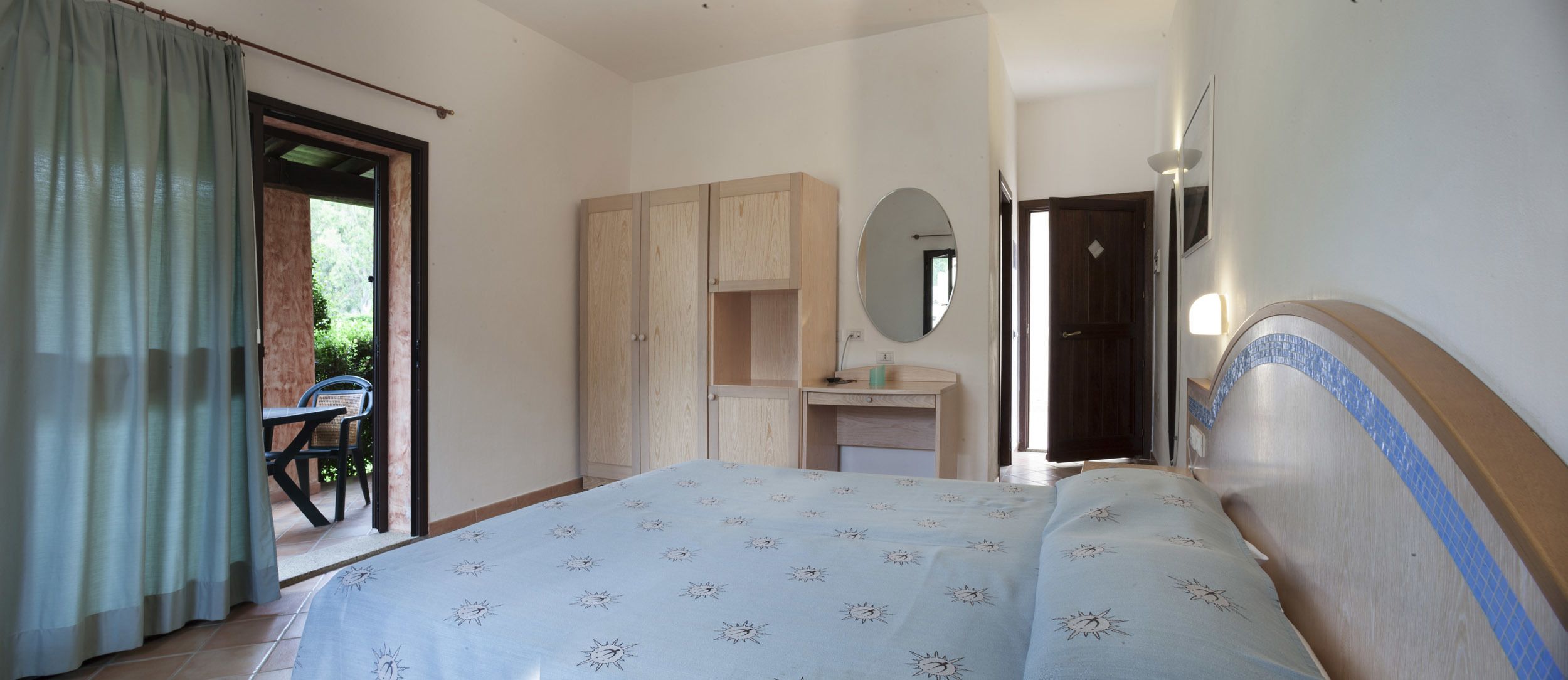 Un dormitorio con cama, armario, espejo y un pequeño escritorio.