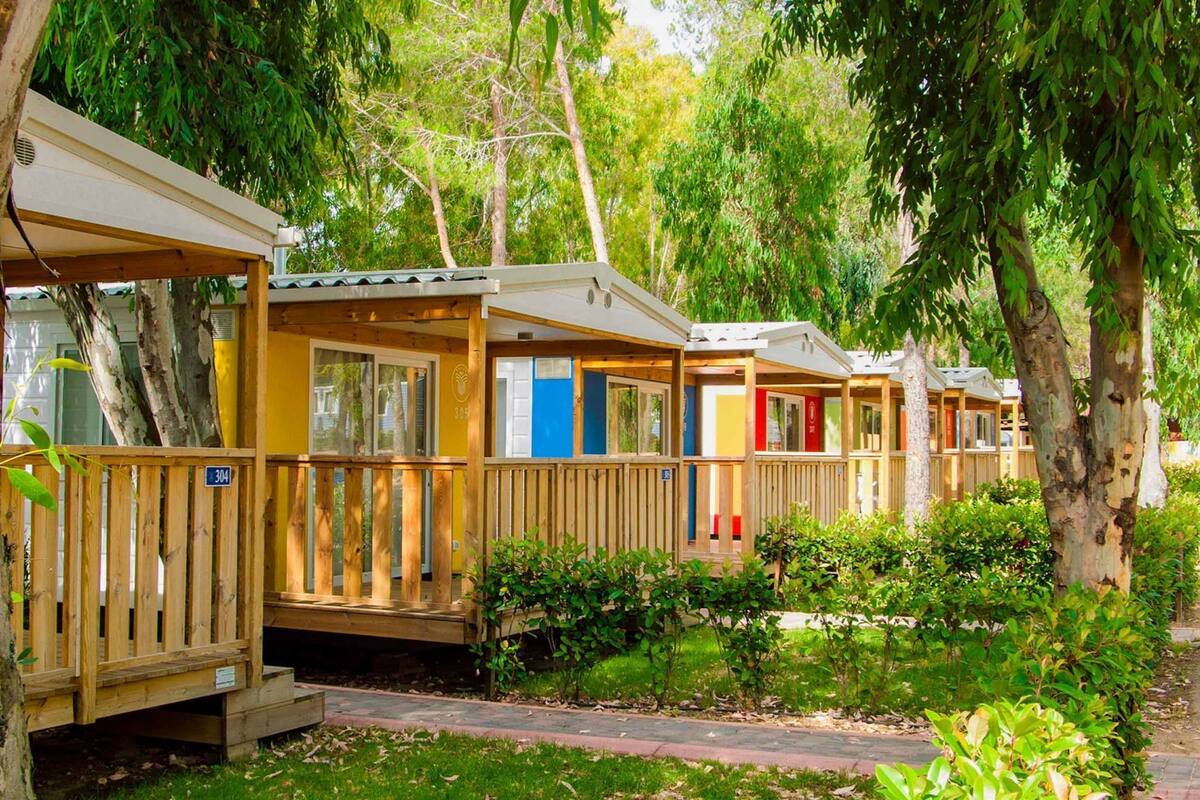 Una hilera de casas móviles de madera con balcones, rodeadas de árboles y vegetación.
