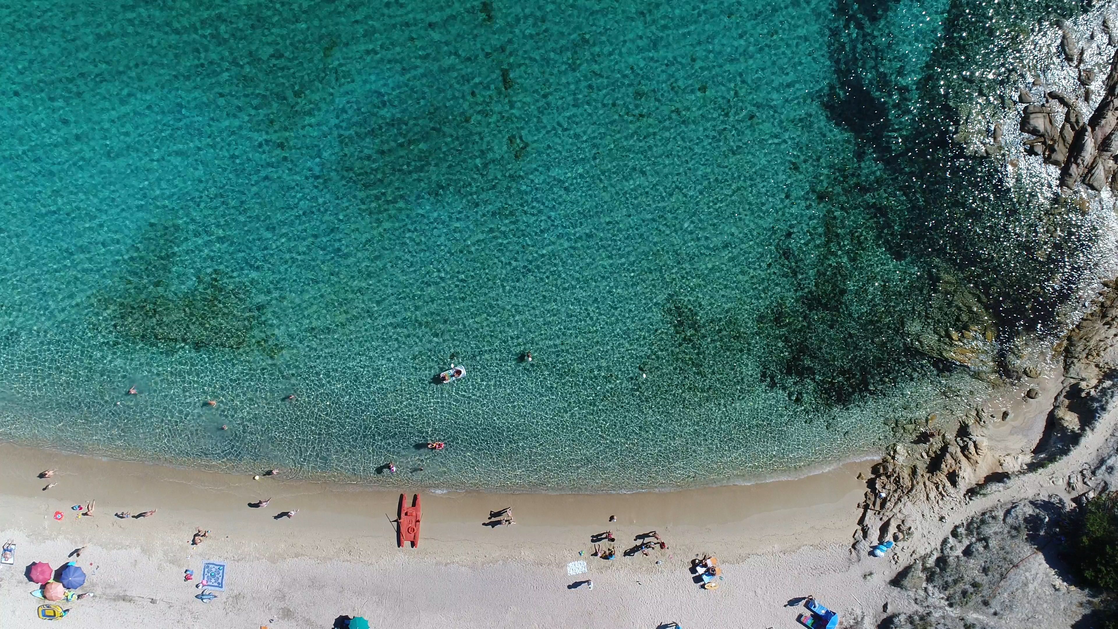 An aerial view of a beach with clear turquoise water, sandy shore, and rocky cliffs.