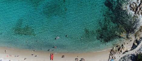 An aerial view of a beach with clear turquoise water, sandy shore, and rocky cliffs.