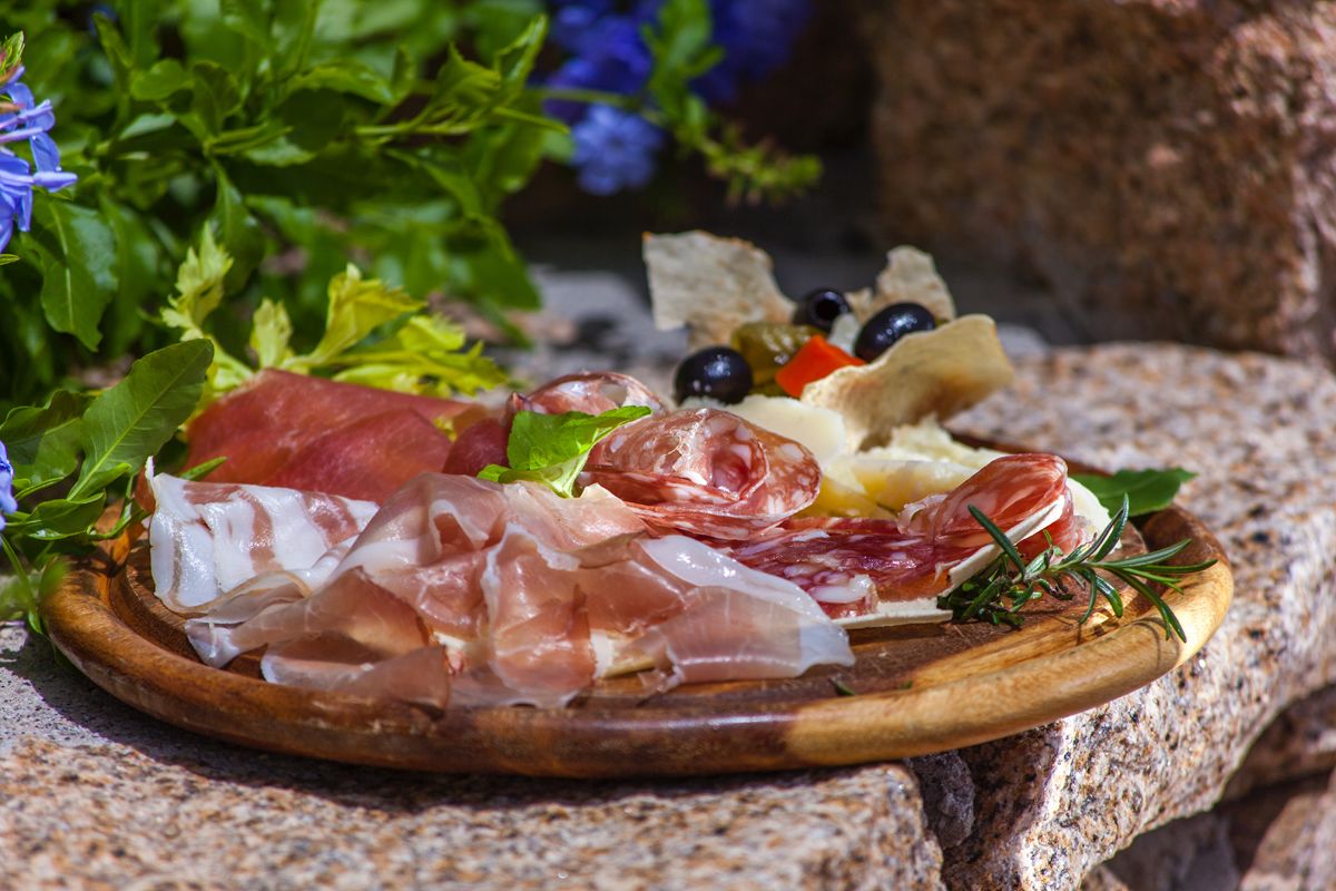 A charcuterie board with various meats, cheeses, olives, and bread on a wooden board.