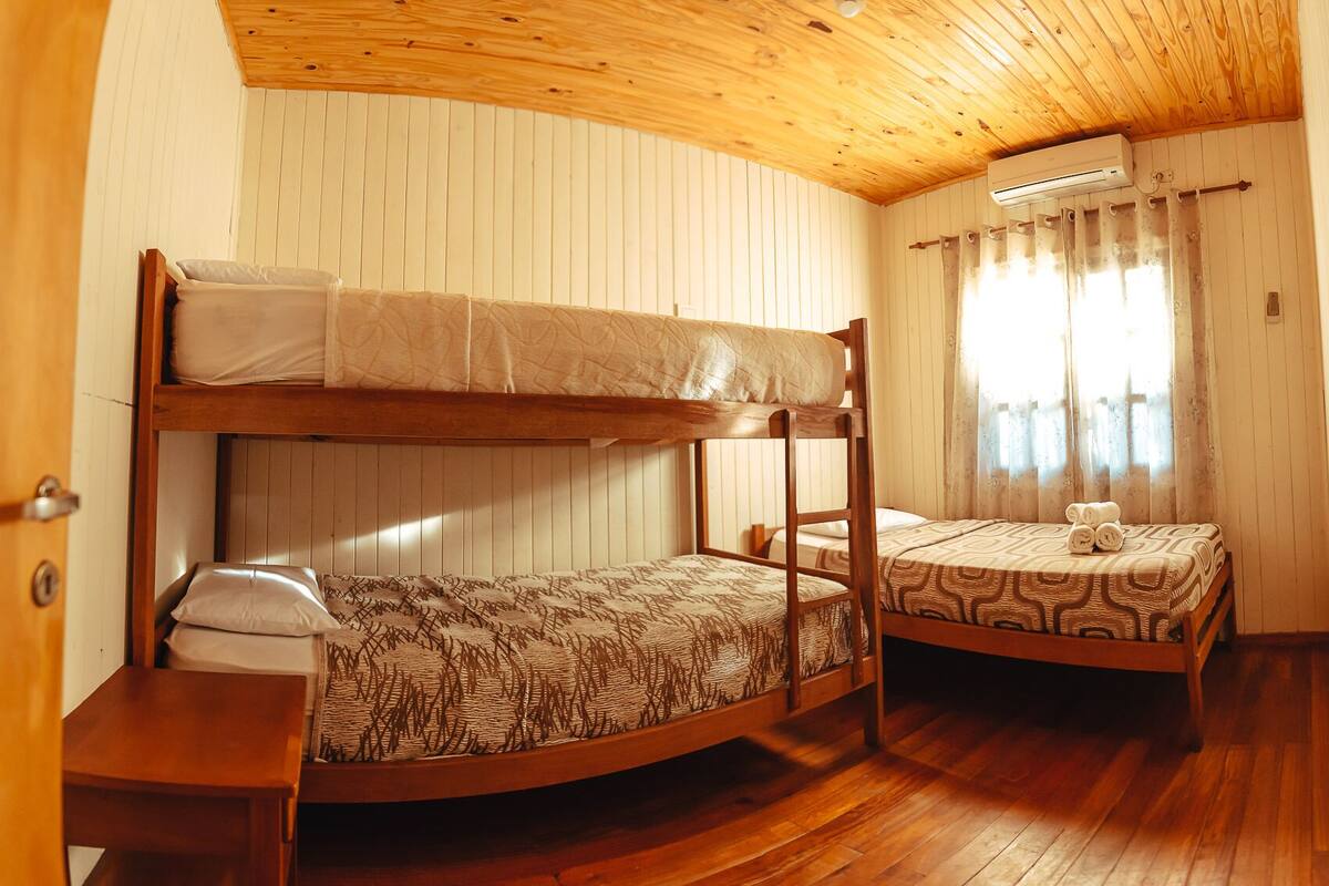 A bunk bed room with a wooden ceiling, a small table, and a window with curtains.