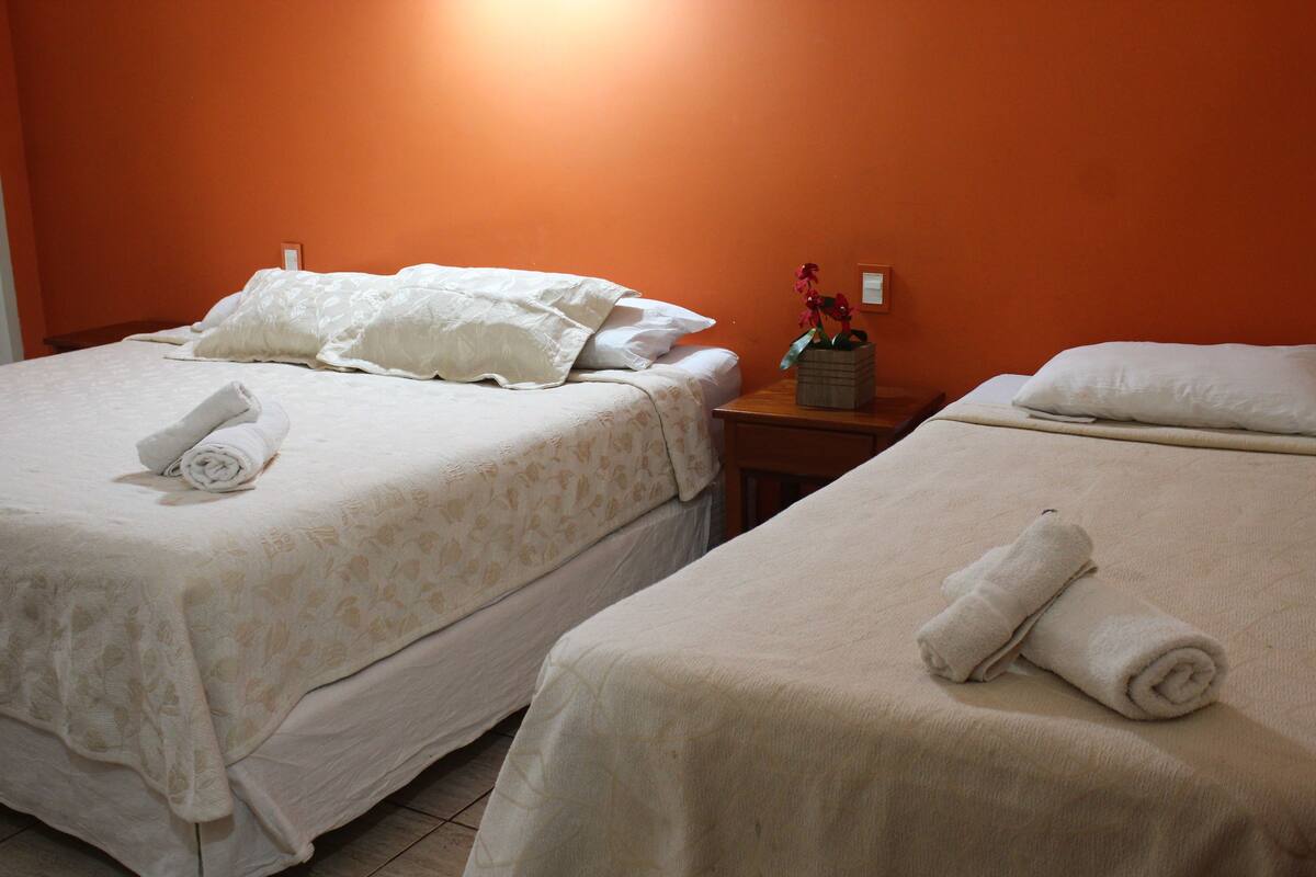 A hotel room with two beds, each with a rolled towel and a vase with flowers on the nightstand.