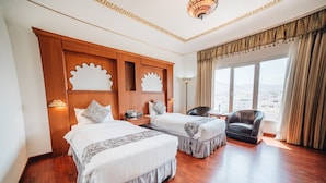A hotel room with two beds, a desk, a chair, and a large window with a view.