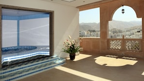 A spacious balcony with a view of a cityscape and mountains, a tiled pool area, and a potted plant.