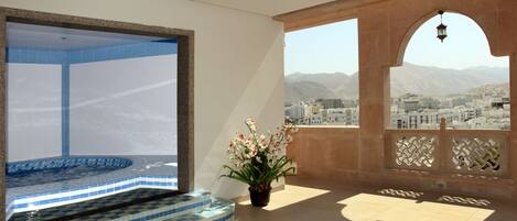 A spacious balcony with a view of a cityscape and mountains, a tiled pool area, and a potted plant.