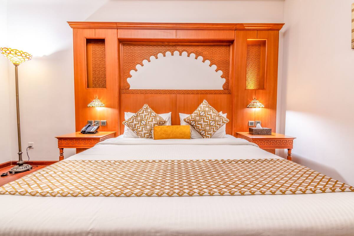 A hotel room with a large bed, two nightstands, a telephone, and decorative lamps.