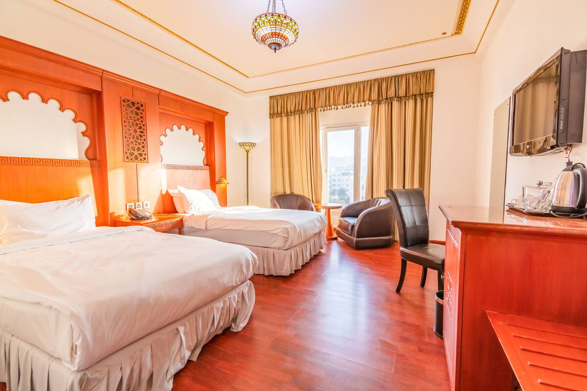A hotel room with two beds, a TV, a desk, a chair, and a view of the city.