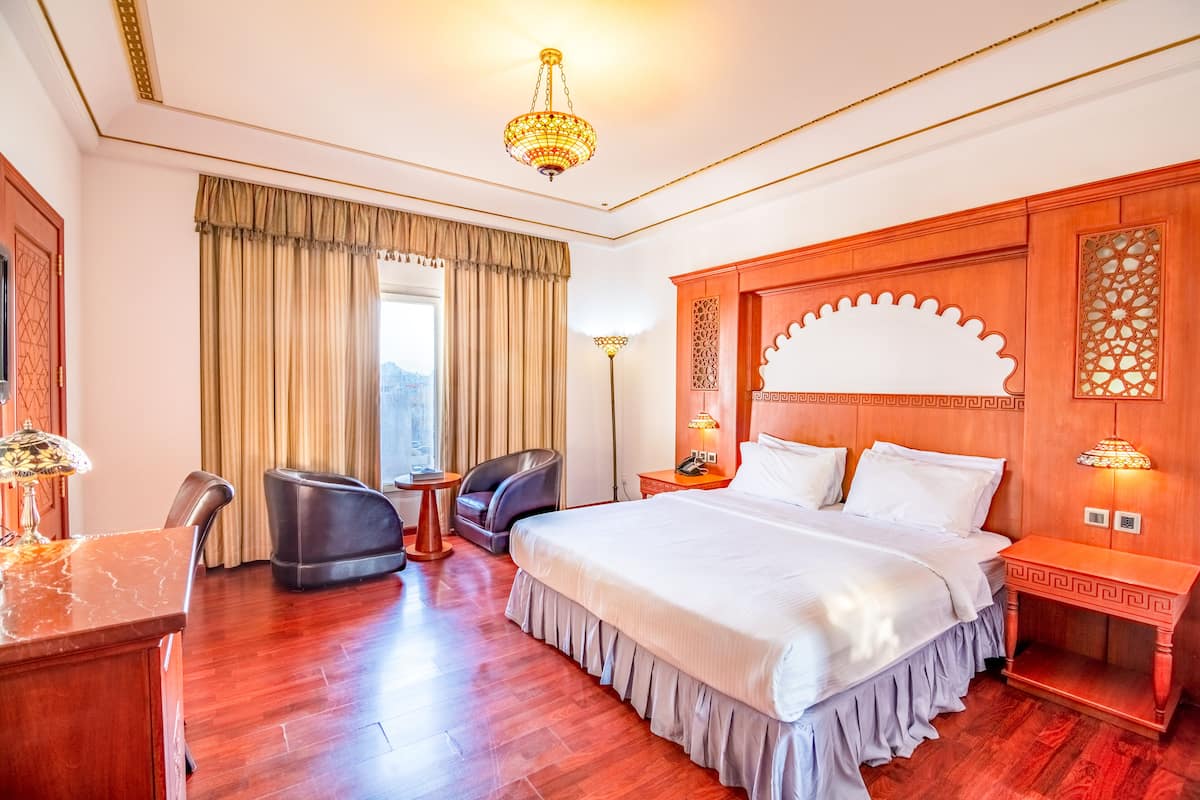 A hotel room with a large bed, two chairs, a desk, and a chandelier.