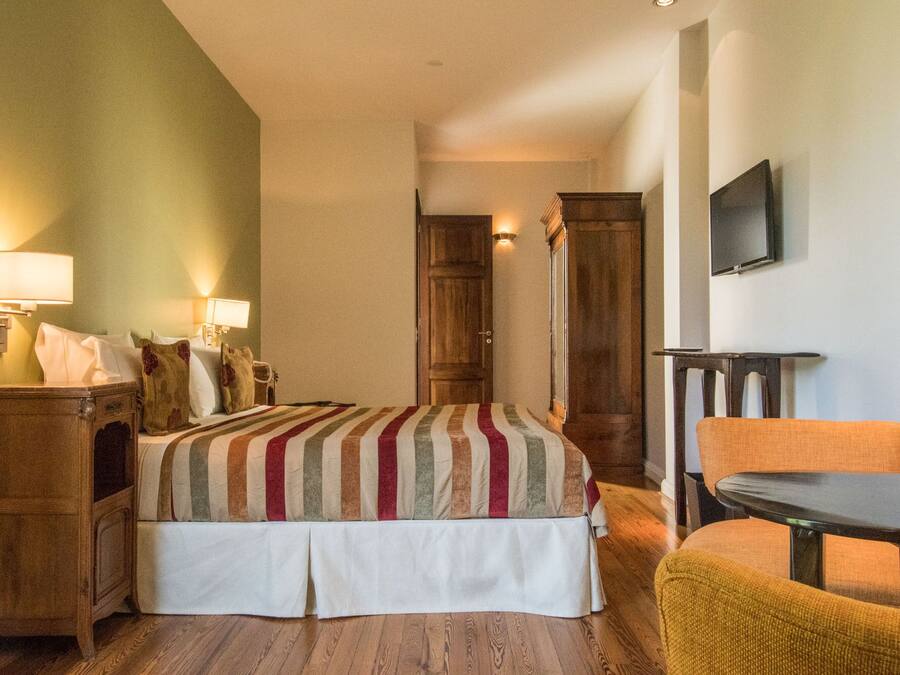 A hotel room with a bed, bedside tables, a chair, a TV, and a wooden wardrobe.