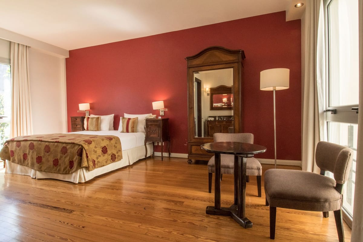 A hotel room with a large bed, a desk, a chair, a mirror, and a lamp.
