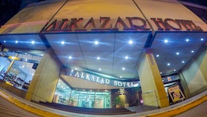 Exterior del Hotel Alkazar, con un cartel llamativo, un acceso cubierto y una escalera visible que conduce a la entrada.