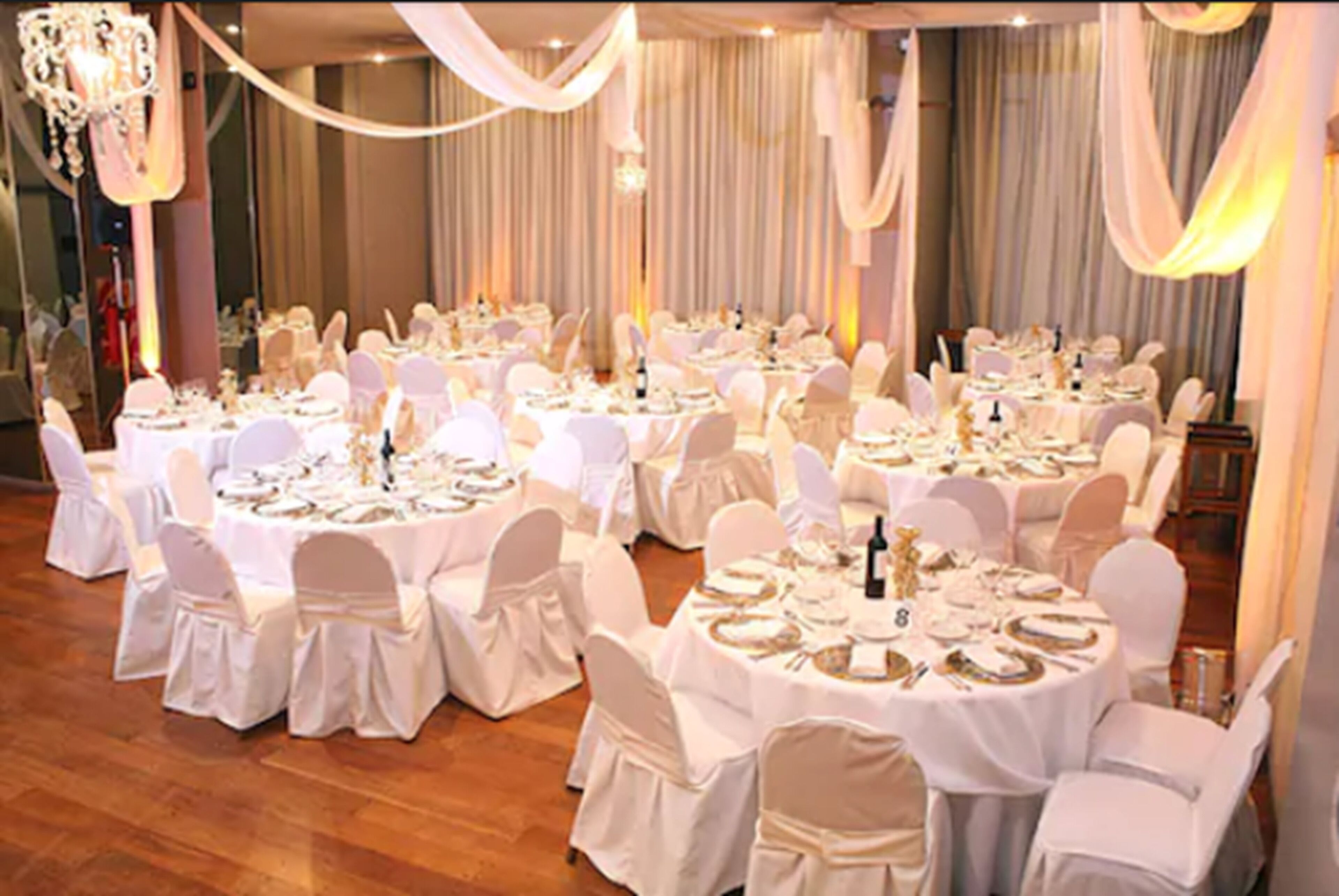 A banquet hall with round tables set for a formal event, draped with white fabric and chandeliers.