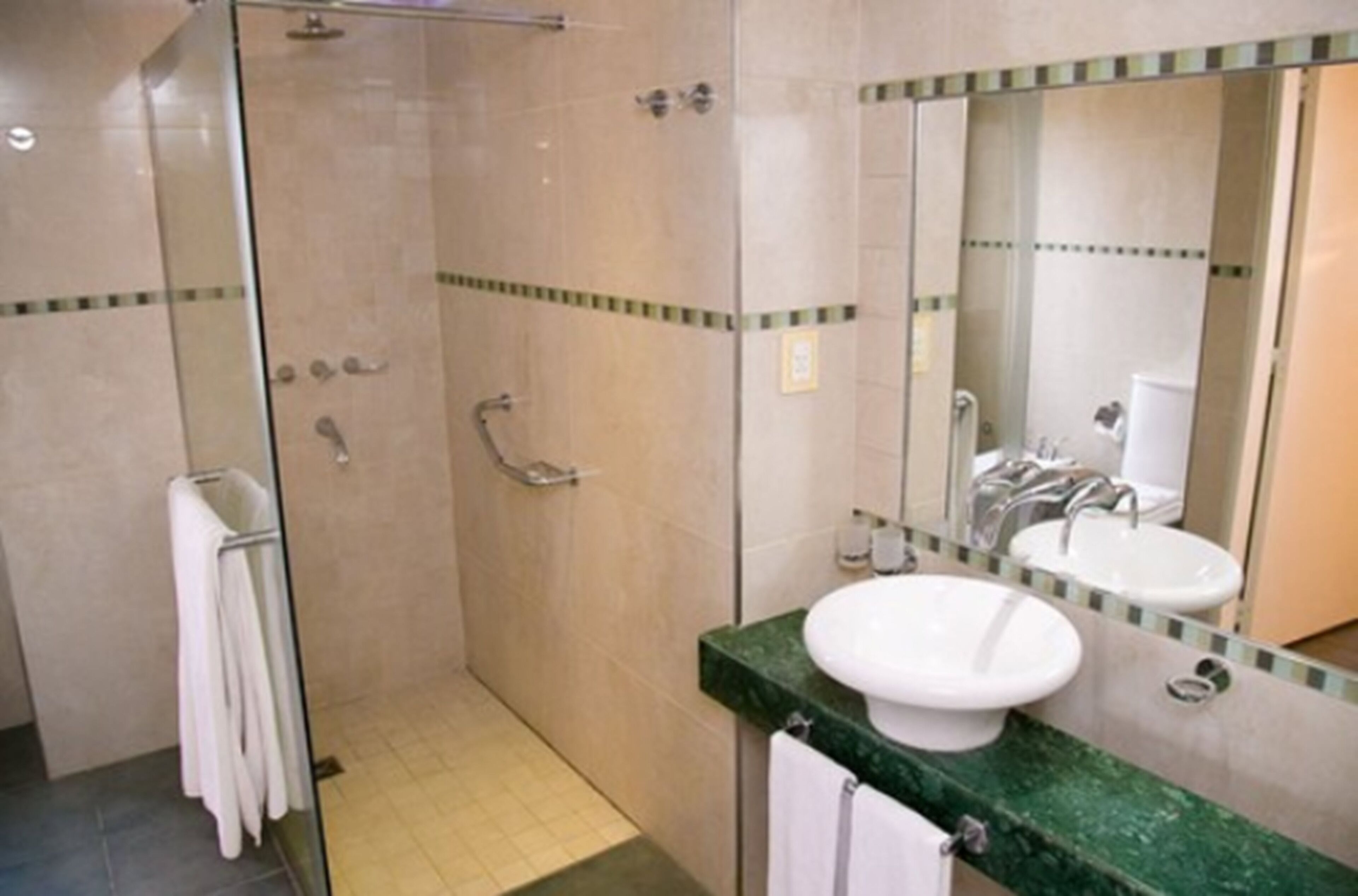 Un bagno con cabina doccia in vetro, lavabo con piano verde e specchio sopra il lavabo.