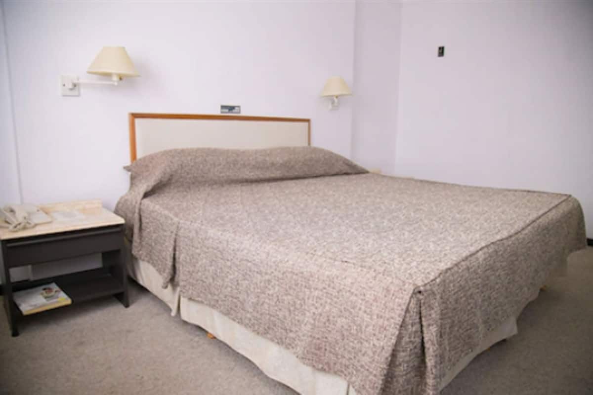 A bedroom with a bed, bedside table, lamp, and a wall clock.