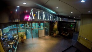 Exterior del HOTEL ALKIZAR con diseño moderno, puertas de vidrio y un área de entrada visible.