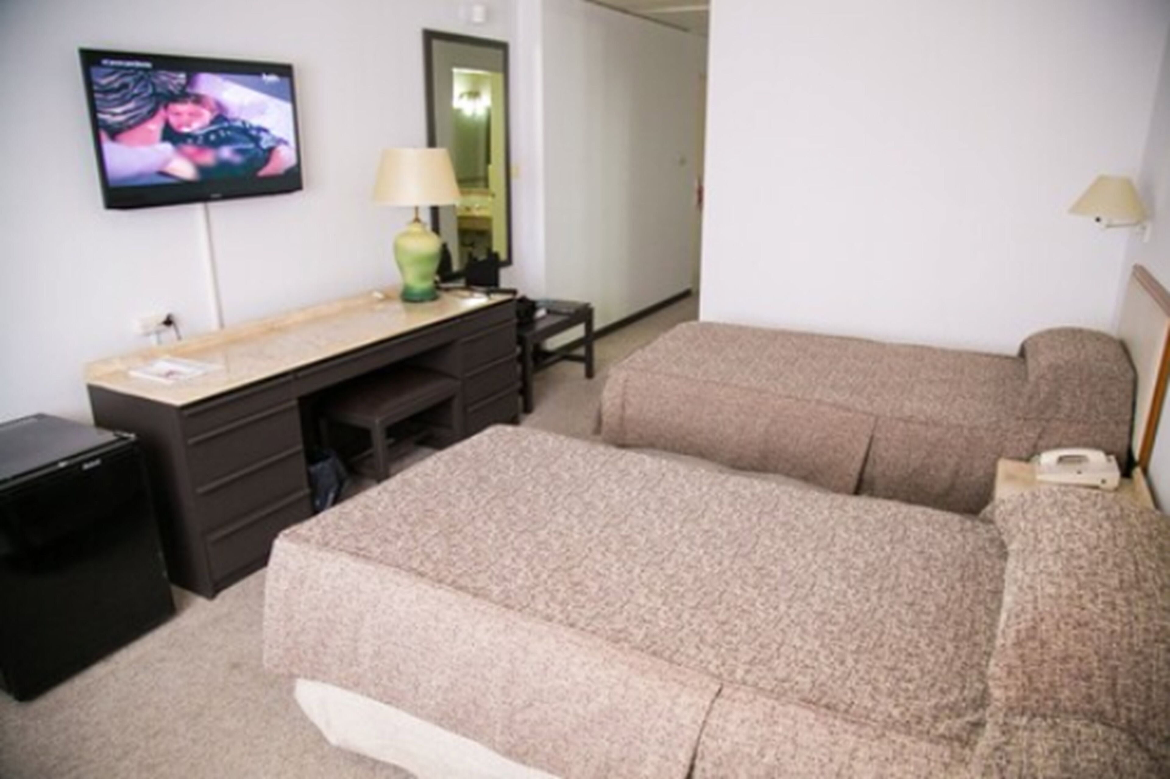 Una habitación de hotel con una cama, un escritorio con lámpara, un televisor y un pequeño armario negro.