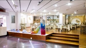 Un amplio vestíbulo de hotel con una escalera central, varias zonas de comedor y una recepción.