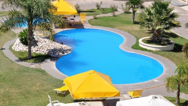 Une piscine entourée de palmiers et de parasols jaunes, avec un chemin de pierre menant à celle-ci.