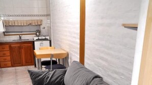 Un espace de vie compact avec un canapé gris, une petite table en bois et, au fond, une kitchenette.