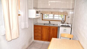 Une cuisine compacte avec des meubles de rangement en bois, un évier, un four à micro-ondes et une petite table.