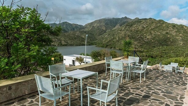 An outdoor patio with stone flooring and metal chairs and tables, overlooking a lake and mountains. - Hostería y Cabañas Valle Fertil (San Agustin de Valle Fertil)