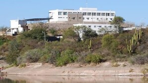 A building with a flat roof and multiple windows, surrounded by sparse vegetation and a body of water. - Hostería y Cabañas Valle Fertil (San Agustin de Valle Fertil)
