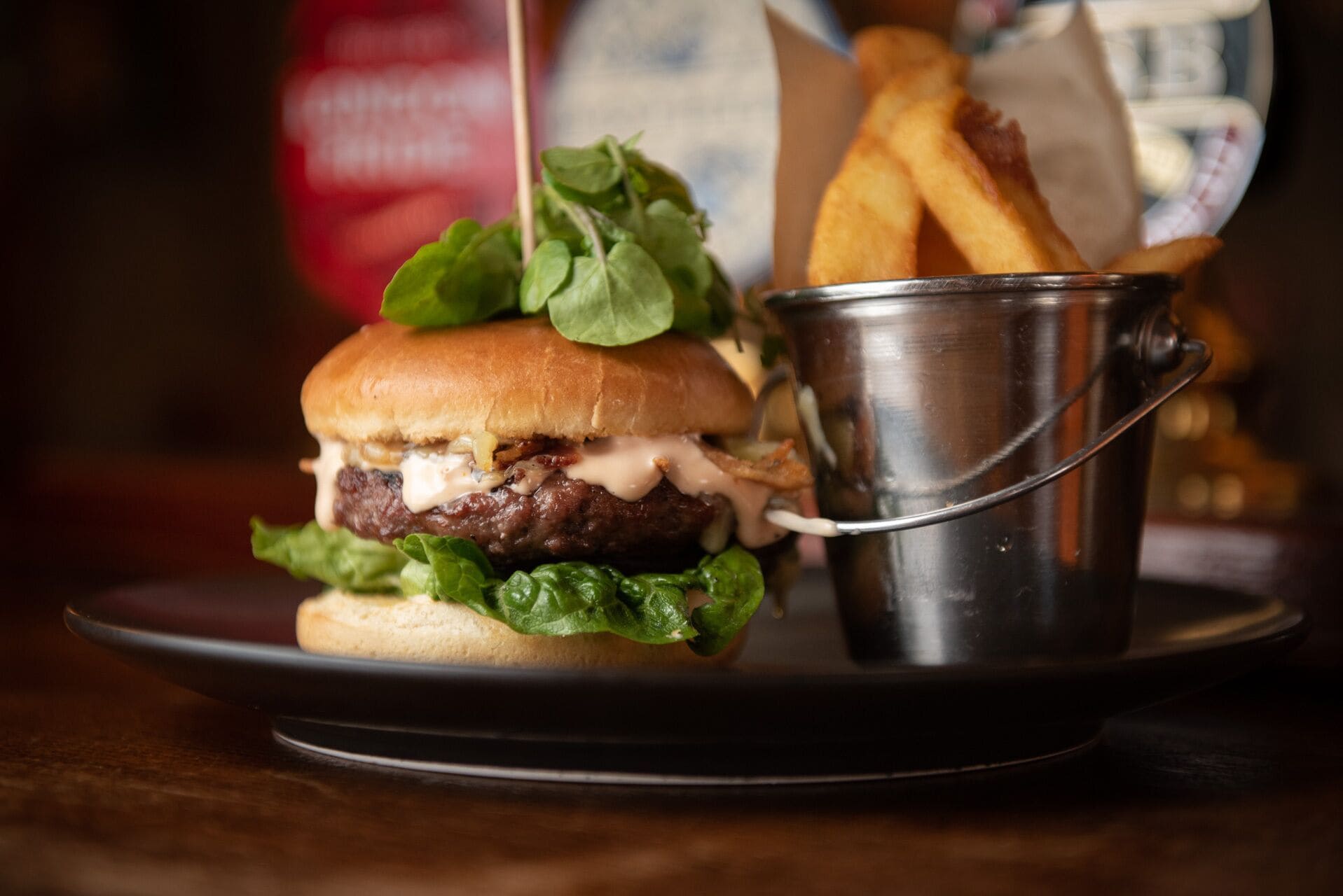 Una hamburguesa con lechuga y papas fritas en un vaso de metal sobre un plato.