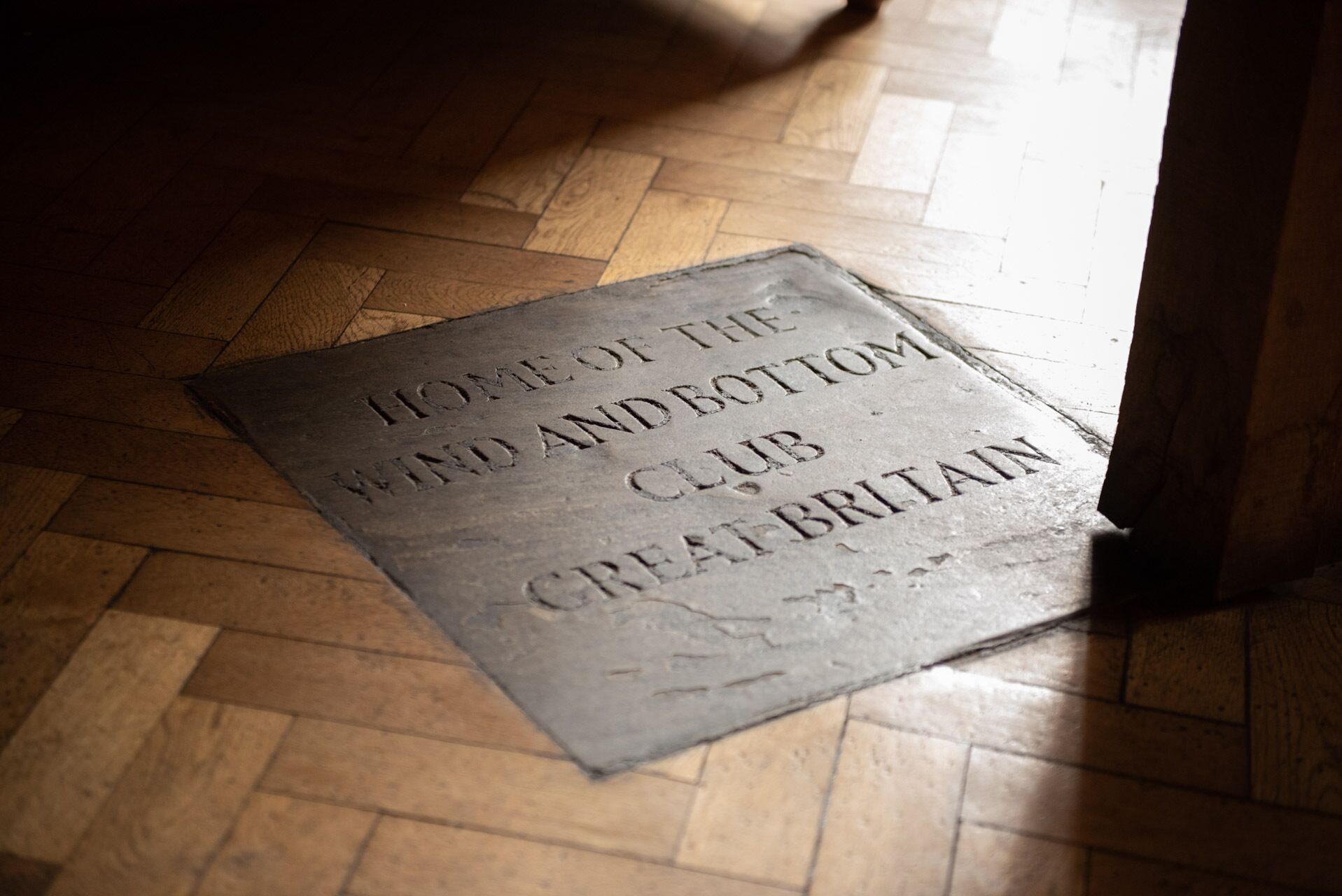 Una placa de piedra sobre un suelo de madera con la inscripción “HOME OF THE WIND AND BOTTOM CLUB GREAT BRITAIN”.