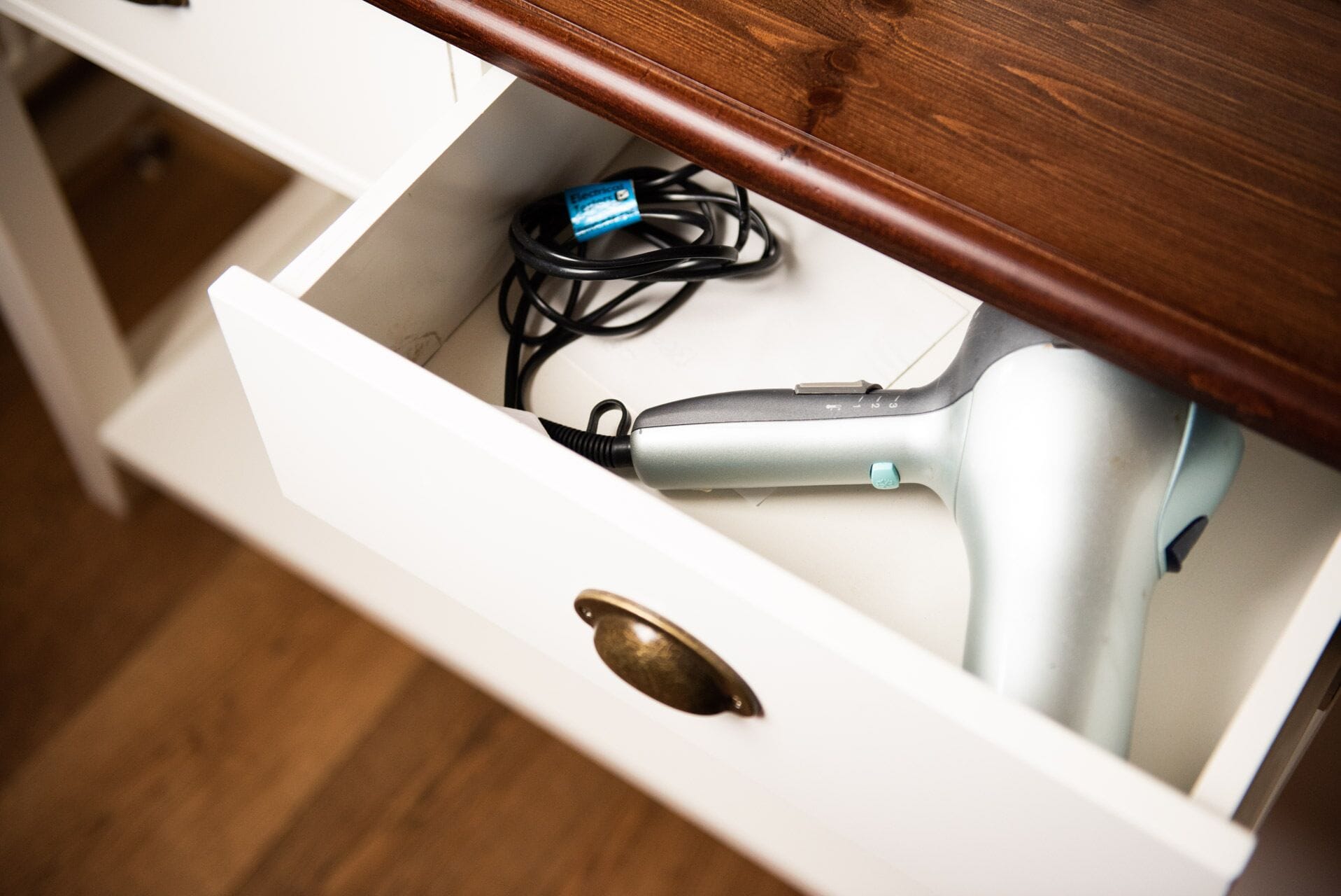 A drawer with a hairdryer and a power cord inside.