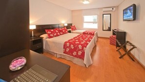 Habitación de hotel con dos camas, un escritorio con una computadora portátil, un televisor y una mesita con un frutero.