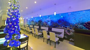 Un restaurante con una pared de acuario, sillas y mesas blancas.