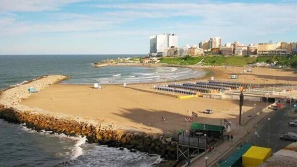 Una playa costera con un litoral rocoso, una zona de arena y una fila de edificios al fondo.