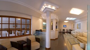 Un moderno vestíbulo de hotel con mostrador de recepción, zona de estar y una pantalla de televisión.
