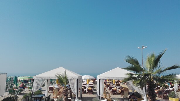 A beachside resort with multiple white tents, sun loungers, and palm trees. - Albion Hotel (Golem)