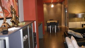 A modern living room with a sofa, a dining area with a table and chairs, and a kitchen area with a counter and decorative items. - Albion Hotel (Golem)