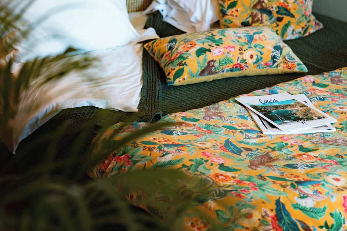 Een hotelkamer met twee bedden, een nachtkastje met een lamp, een hoed en een bloempot.