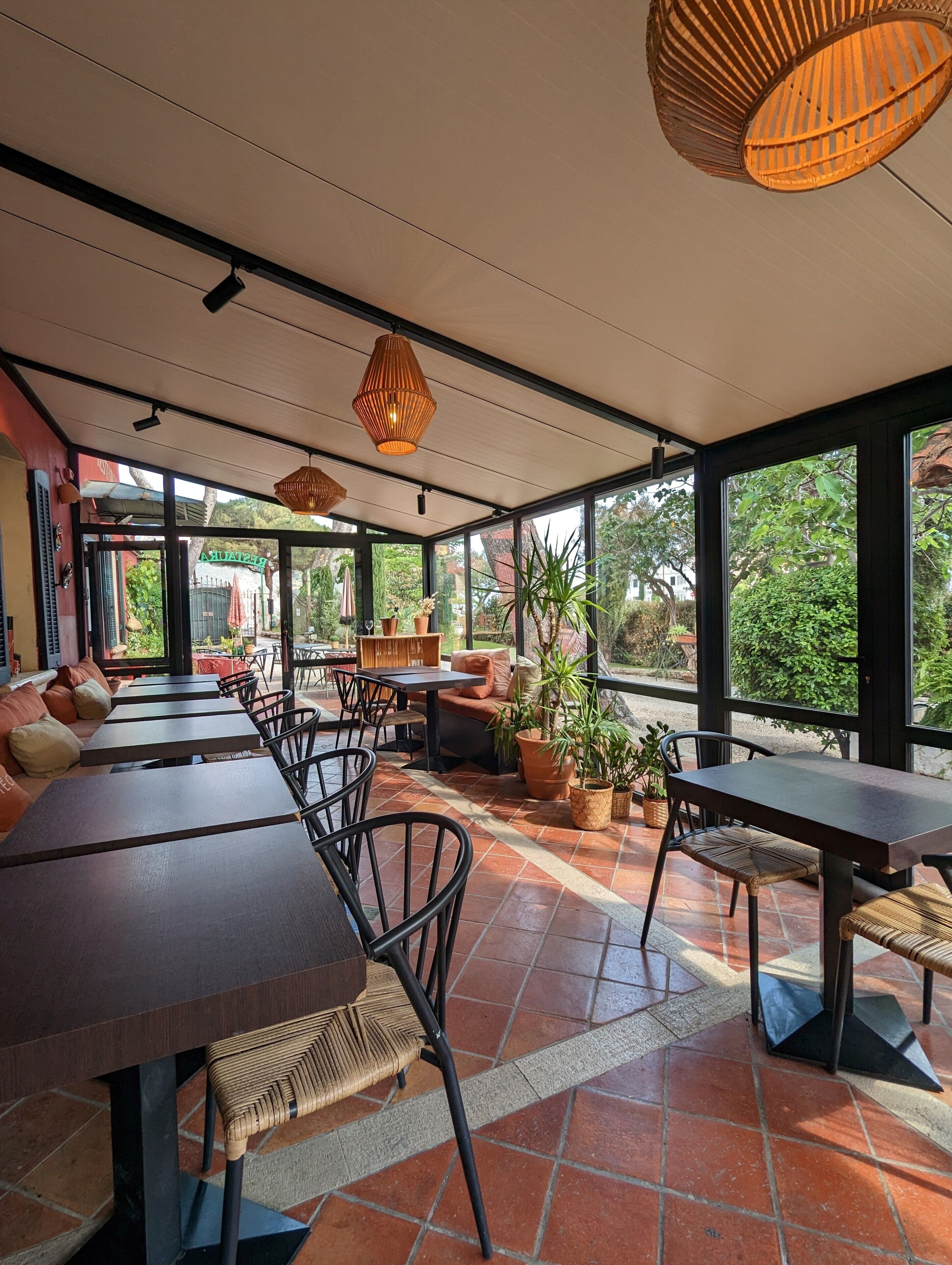 A restaurant with outdoor seating, large windows, and hanging wicker lamps.
