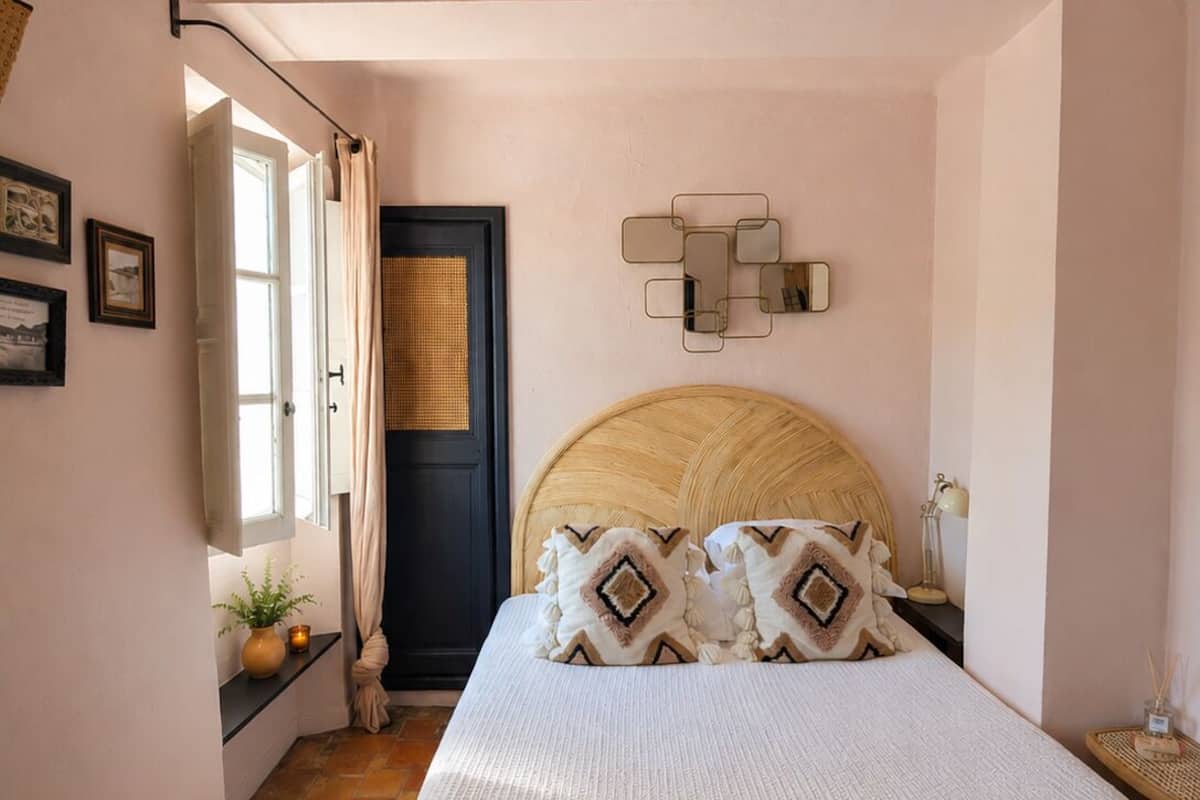 Een slaapkamer met een bed, een deur, een wandlamp en een raam.