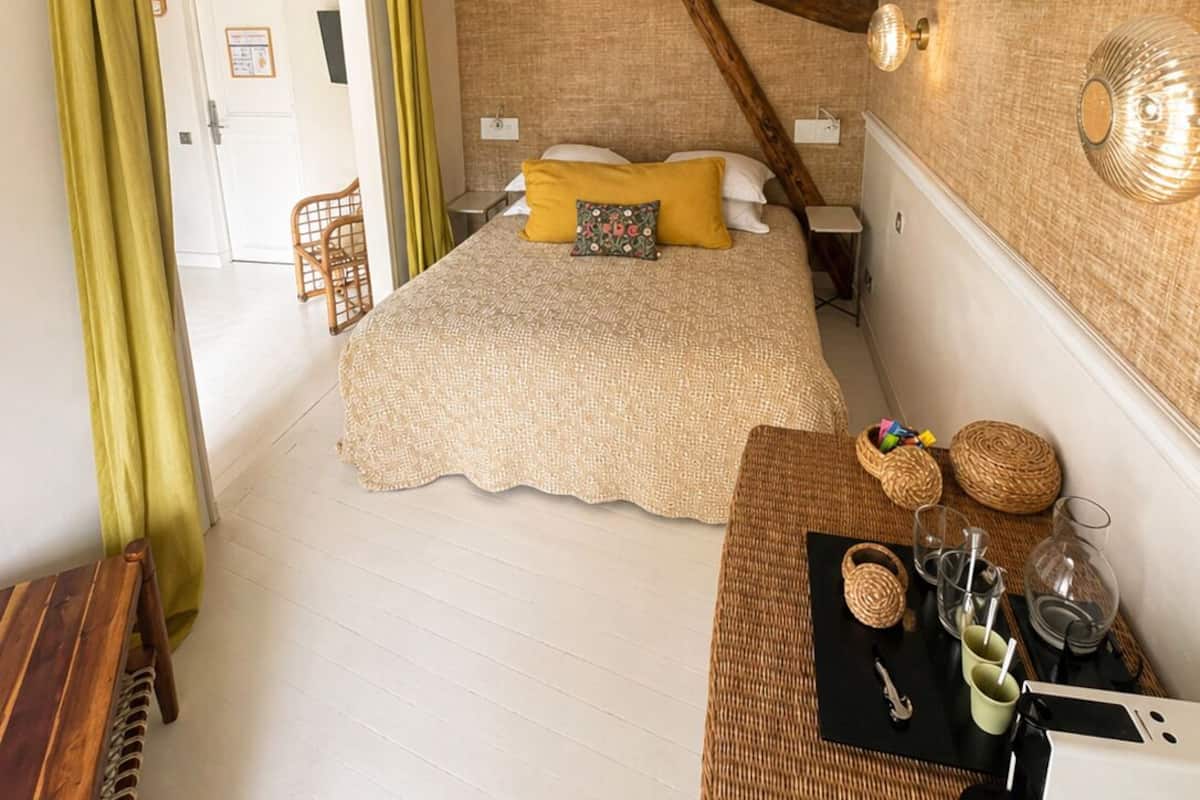 Een slaapkamer met een bed, een houten bankje, een tafel met glazen en een doos, en een rieten mand.