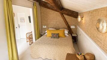 Une chambre à coucher avec un lit, un banc en bois, une table avec des verres et une boîte, et un panier en osier.