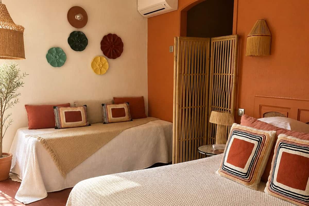 Een hotelkamer met twee bedden, een potplant, een wandairconditioner en een bamboescherm.